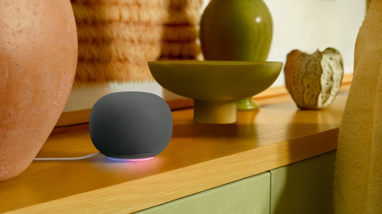 Tampak samping Google Home Speaker dengan kabel充电 terpasang, menunjukkan siluet ringkas cocok untuk meja kerja atau nakas